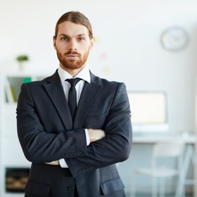 Business employee Young bearded business employee in elegant suit crossing arms on chest while standing in front of camera
